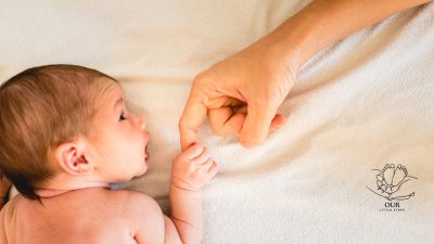 A tired but happy new parent holding a newborn baby at home, surrounded by essential baby items like diapers and bottles