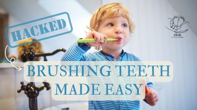 A smiling baby holding a soft toothbrush while a parent gently helps with brushing, promoting early oral hygiene habits.
